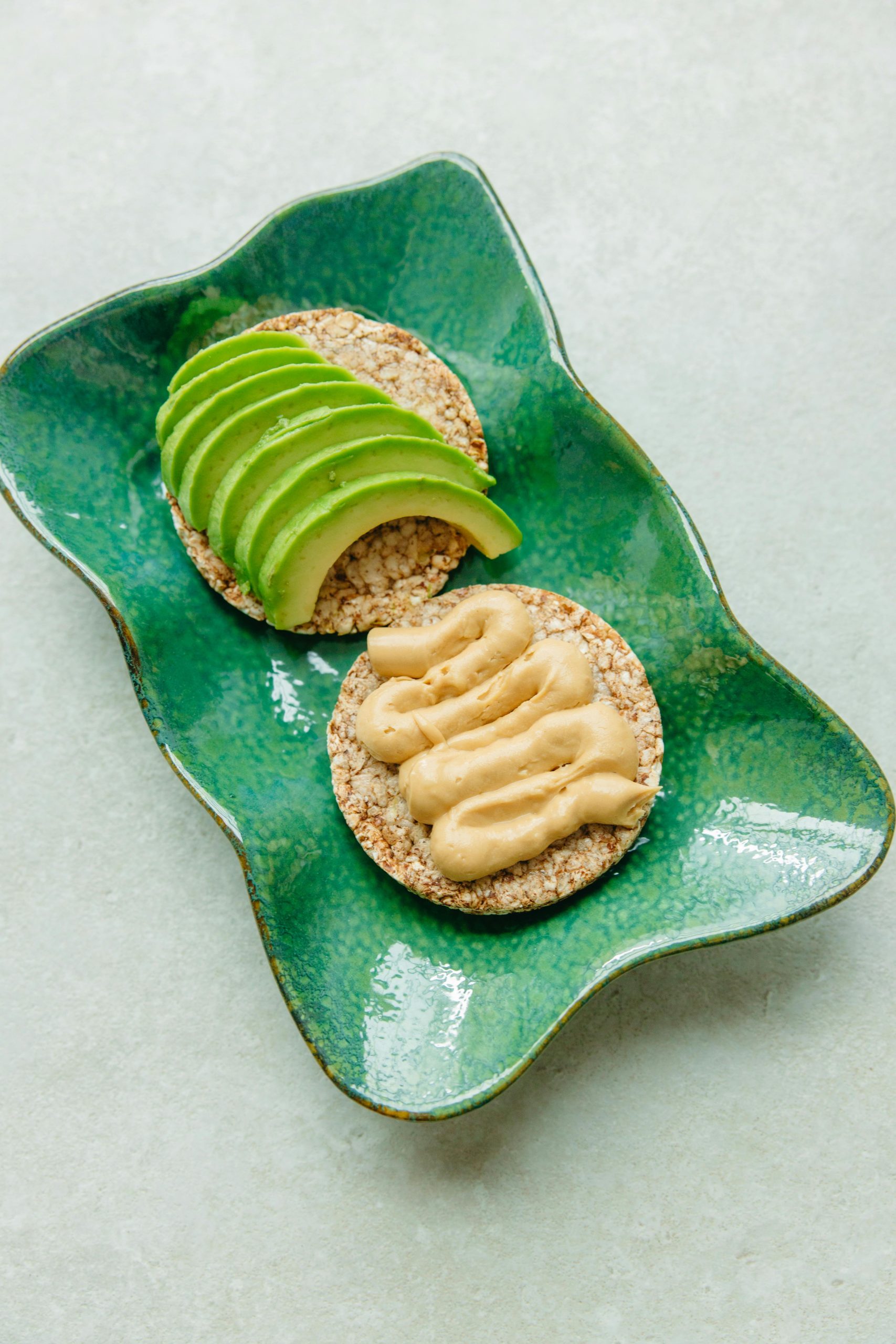 Sliced avocado and hummus on rice cakes served on a ceramic plate for a nutritious snack.